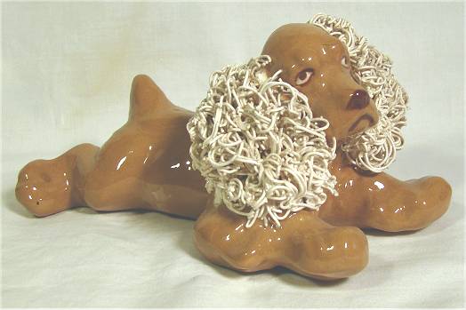 Brown spaniel figurine by Jane Callender with white ears, lying on belly.